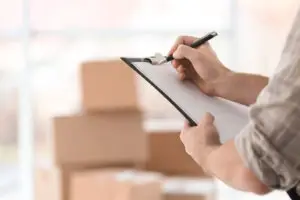 man writing on clipboard with moving boxes behind him