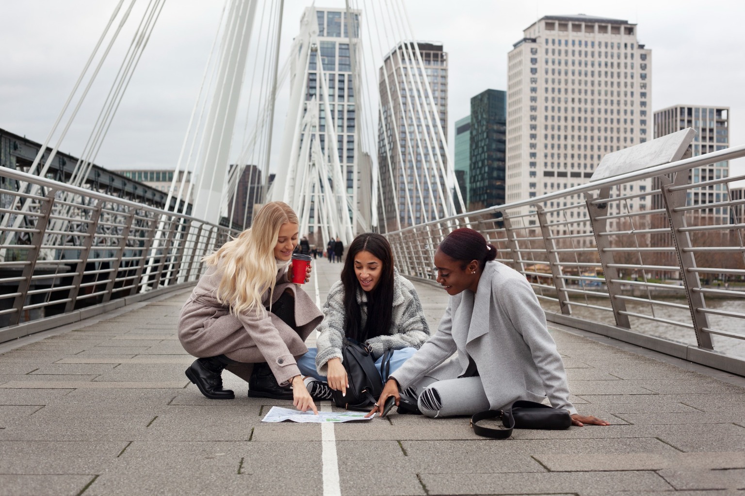 Three friends sitting on a bridge in a new city looking at a map together